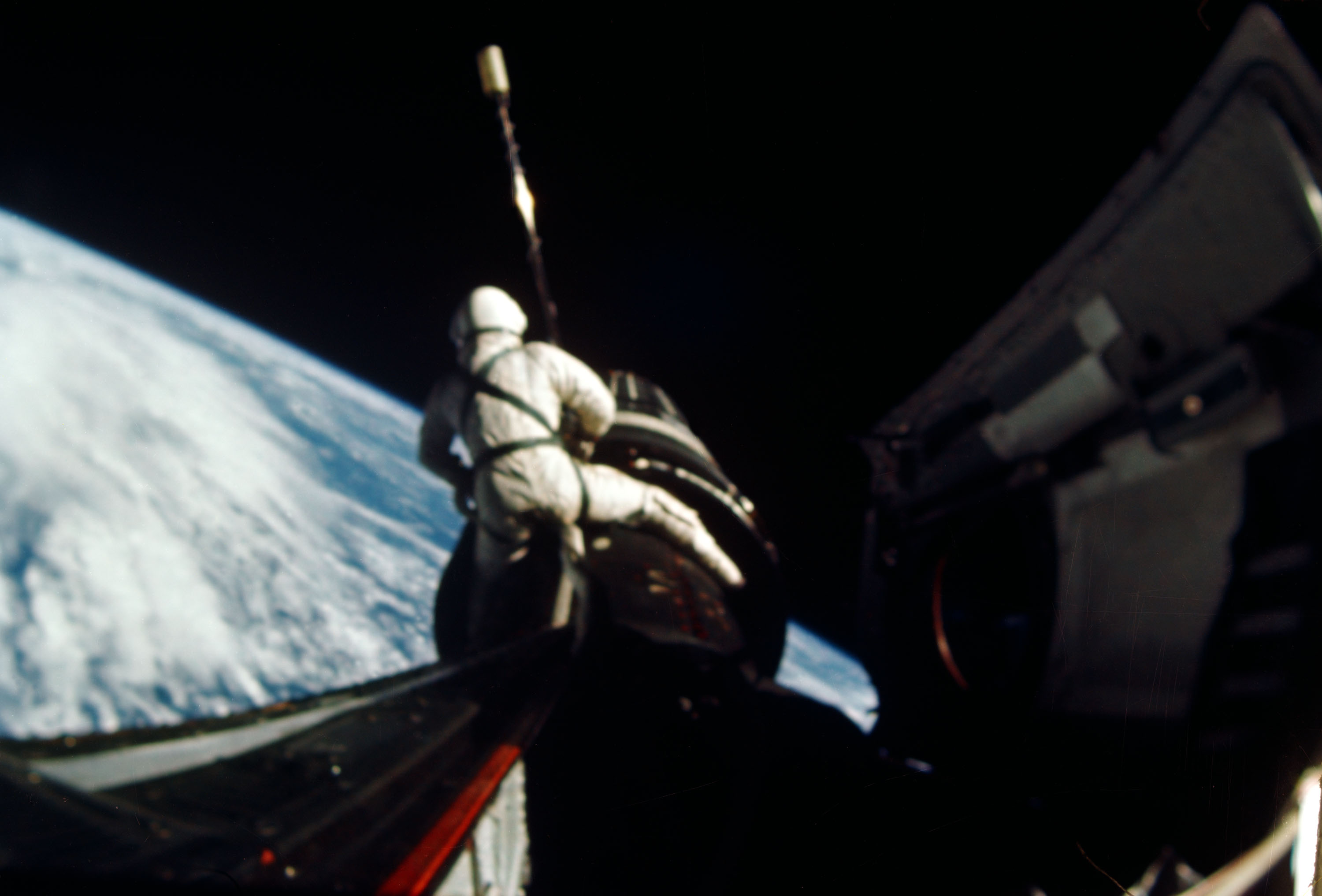 Astronaut Dick Gordon attaches a tether line from his Gemini 11 spacecraft to the Agena target vehicle during a spacewalk.