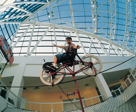 Aided by physics, a boy with outstretched arms balances a bike on a wire.