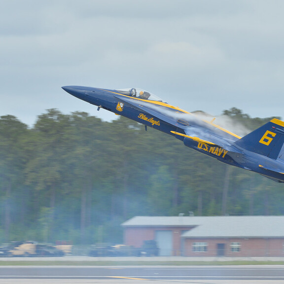 Blue Angels F/A-18 Hornet flying low, showing vortices over its wings