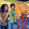 A woman and boy look through an oversized dog-head sculpture to "see like a dog"