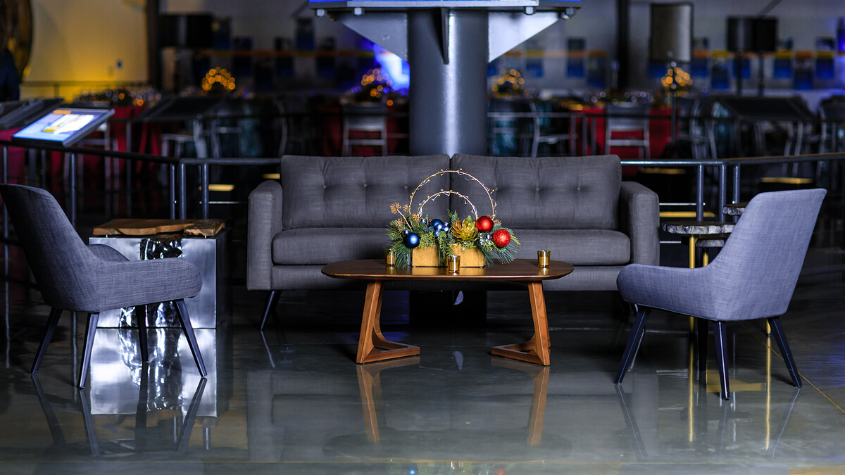 Midcentury Modern grey lounge vignette underneath space shuttle Endeavour for a Holiday Party. A centered coffee table holds a centerpiece decorated with ornaments.