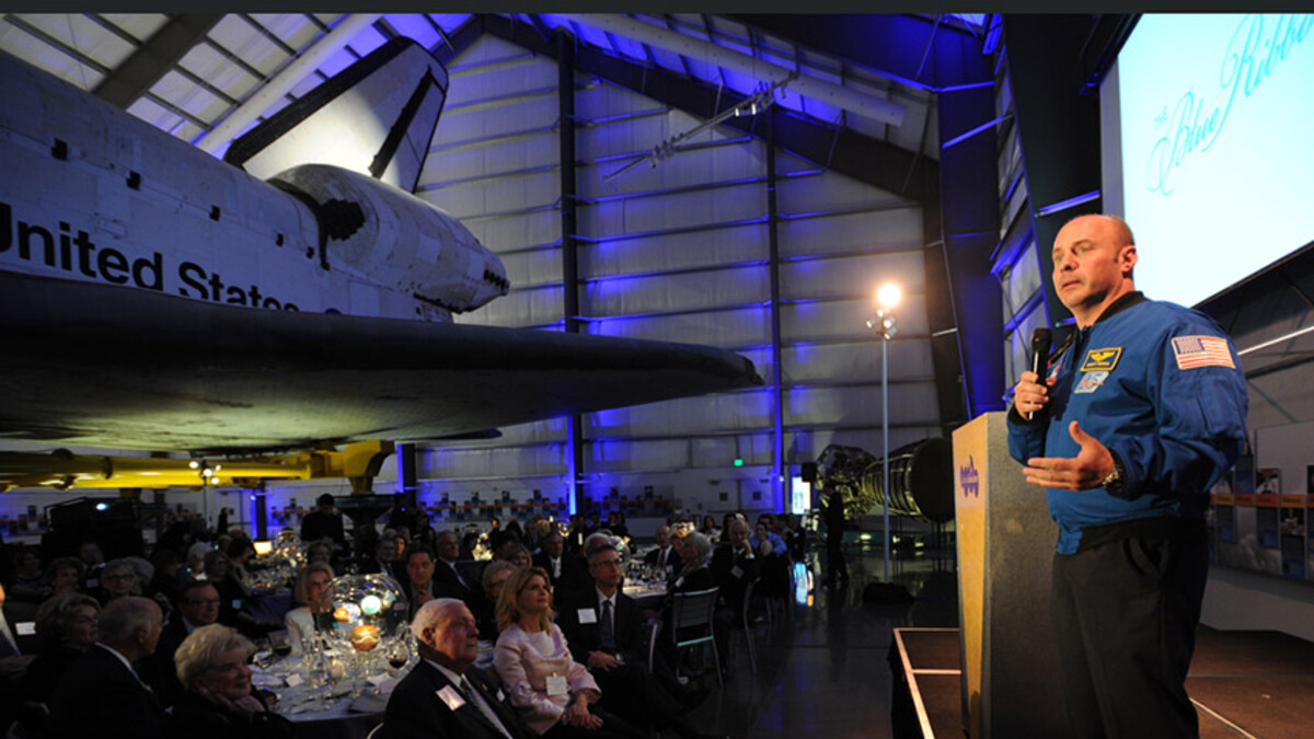 Astronaut Garret Reisman on stage, presenting to gala dinner guests under the space shuttle Endeavour