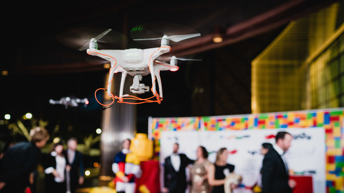 White drone hovers near AOTB Discovery Ball red carpet step & repeat in order to photograph arriving guests