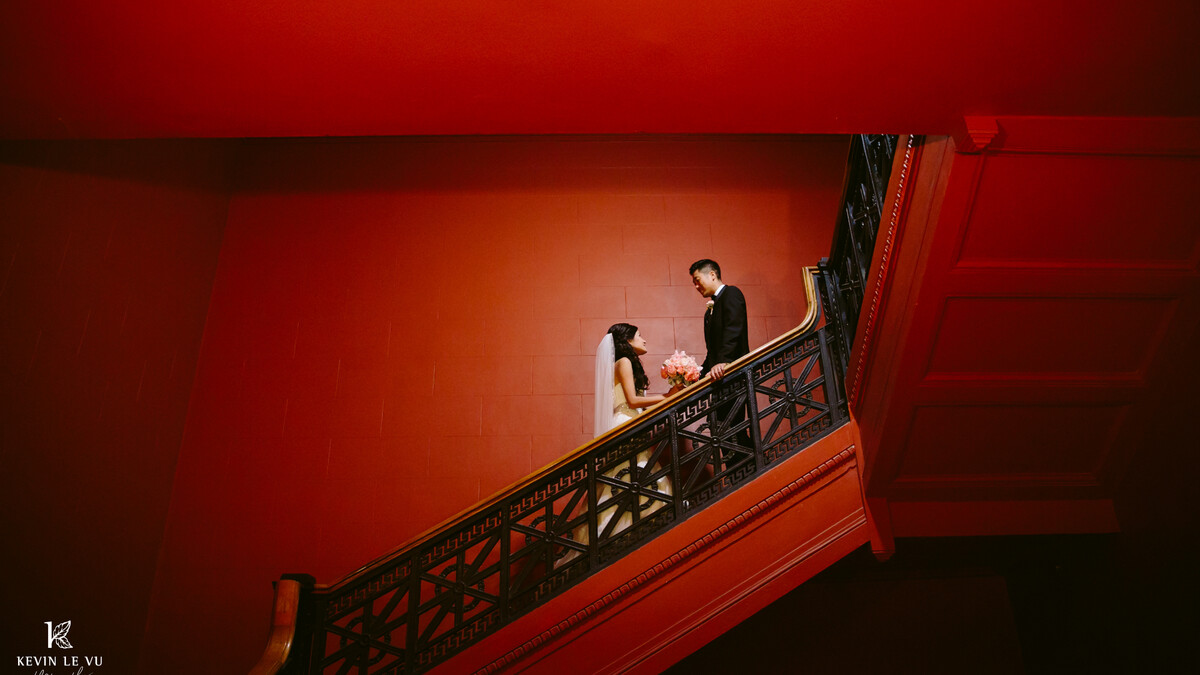 A bride and groom stand facing one another on a burnt orange staircase