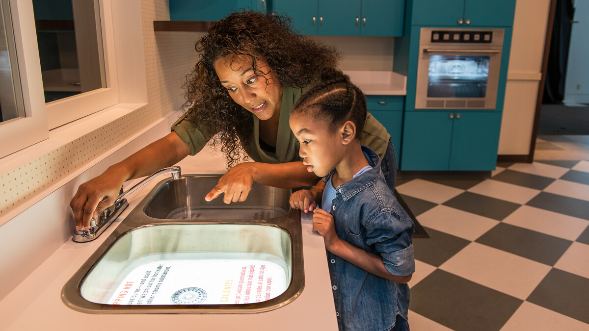 An adult and child read a lit graphic in a kitchen sink.