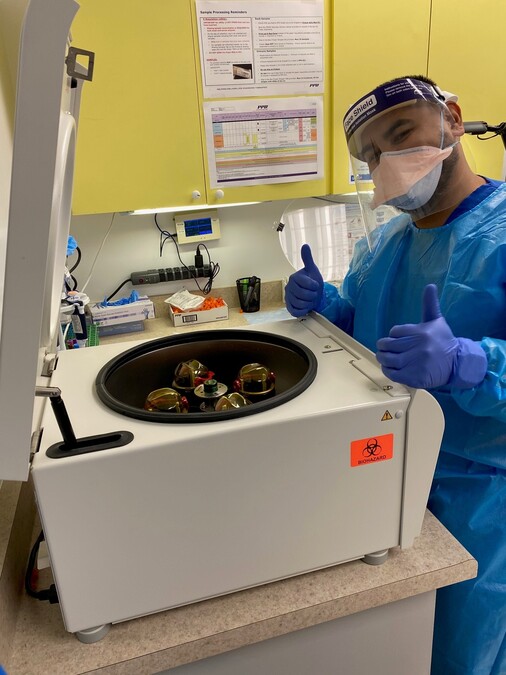 Laboratory technician Jon Veloz flashes a thumbs-up sign as he places samples in a centrifuge at the UCLA Vine St. Clinic