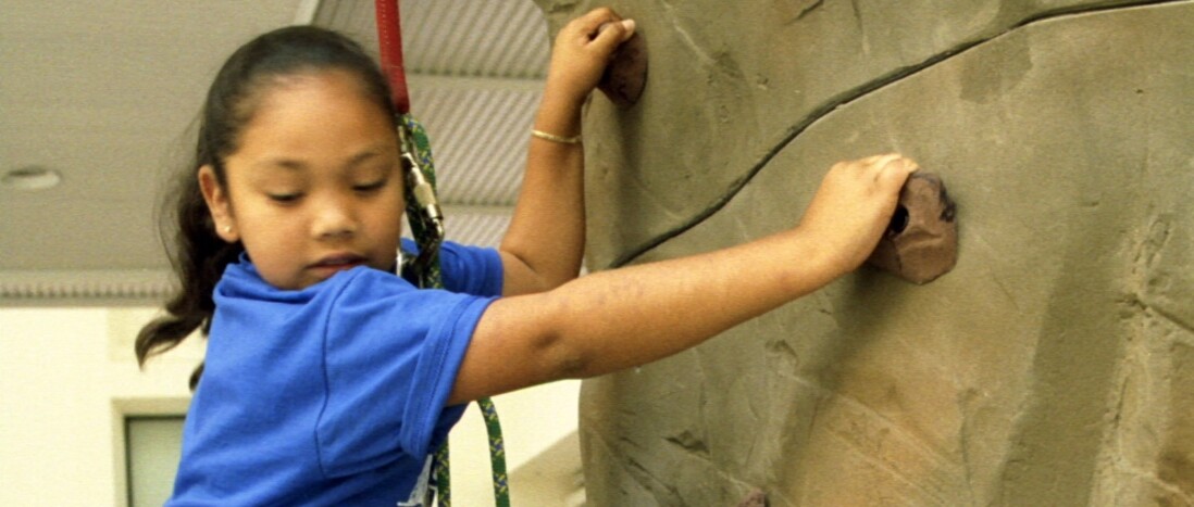 Young girl wearing harness climbs artificial rock wall